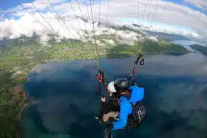 Personne en parapente survolant le lac d'Annecy, souriante et détendue, profitant d'une vue panoramique à couper le souffle.