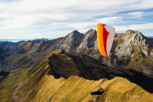 Un pilote de parapente en pleine compétition exécute une manœuvre complexe au-dessus des montagnes, illustrant la précision et l'audace requises dans ce sport aérien exigeant.