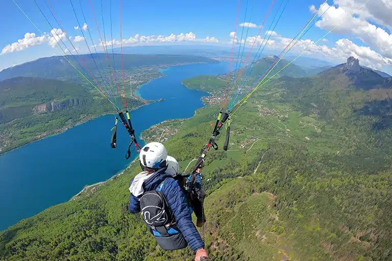 Décollage en parapente au col de la Forclaz à Annecy, avec vue sur le lac turquoise et les montagnes alpines.